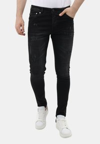 Zwarte slim-fit jeans met versleten details, vijfzakkenontwerp en knoopsluiting. Gecombineerd met witte sneakers voor contrast.