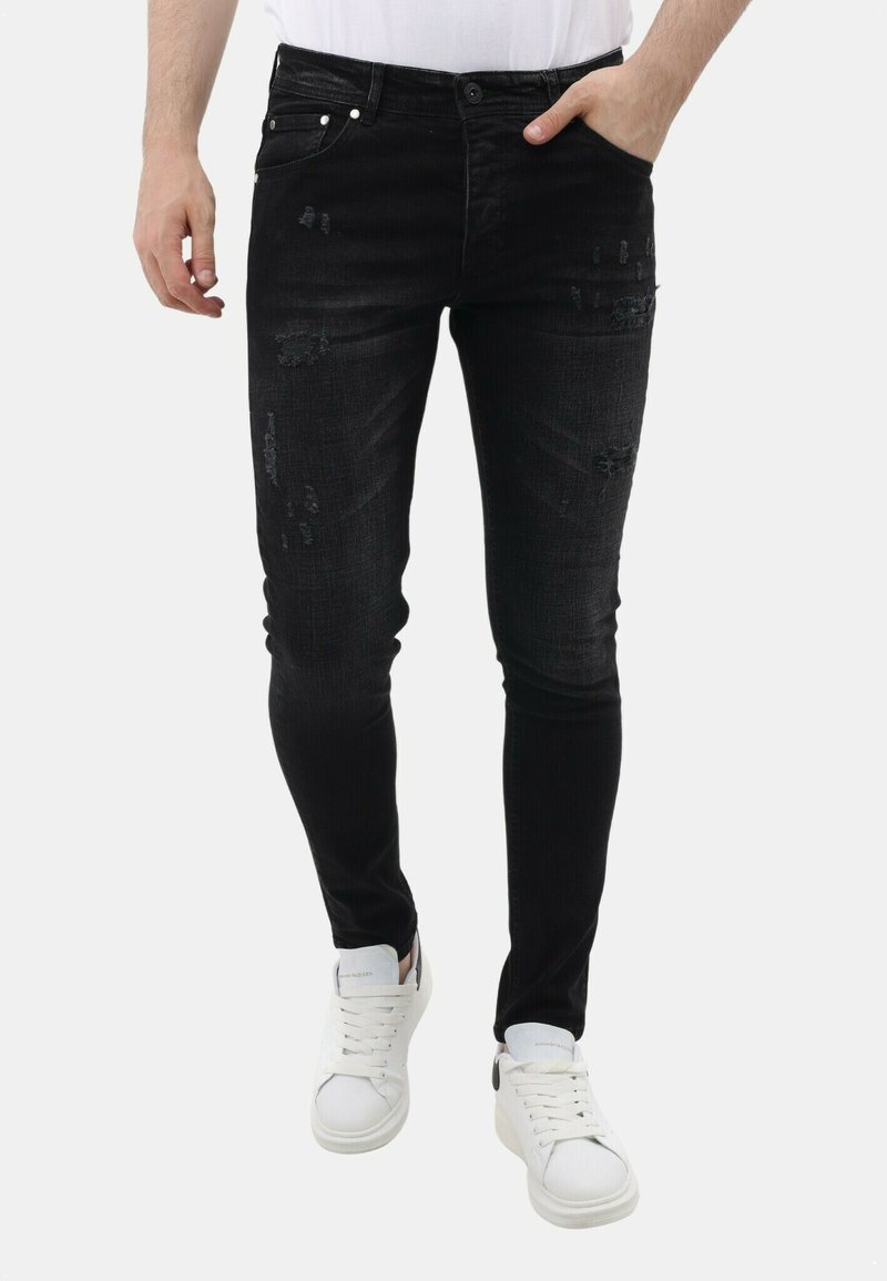 Zwarte slim-fit jeans met versleten details, vijfzakkenontwerp en knoopsluiting. Gecombineerd met witte sneakers voor contrast.
