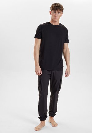 Sort crew-neck t-shirt parret med løstsiddende sorte cargo-bukser med elastiske manchetter og sidelommer. Modellen går barfodet.