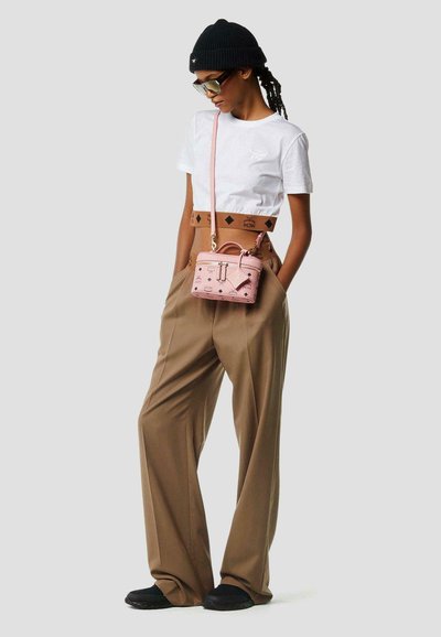 Personne portant un bonnet noir, des lunettes de soleil, un haut blanc court, un pantalon large marron, des chaussures noires, et un petit sac rose porté en bandoulière.