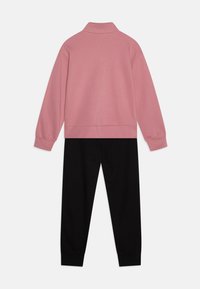 Sweat-shirt rose avec un col montant et un pantalon de survêtement noir. Le matériau semble doux, avec des poignets côtelés aux manches et aux ouvertures des chevilles.