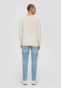 Helles beige Langarmshirt mit Rundhalsausschnitt, kombiniert mit hellblauen Jeans und weißen Sneakers. Das Shirt hat eine strukturierte Oberfläche.