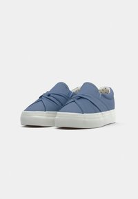 Baskets slip-on en toile bleue avec un design noué à l'avant, semelle en caoutchouc blanche et doublure intérieure à pois.
