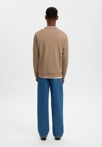 Μπεζ φούτερ με στρογγυλή λαιμόκοψη, μακριά μανίκια και ριμπ τελείωμα· συνοδεύεται από μπλε τζιν παντελόνι φαρδιάς γραμμής με πίσω τσέπες.