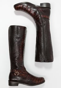 Bottes en cuir marron montant jusqu'aux genoux avec une texture crocodile, dotées d'une fermeture éclair latérale et d'une boucle décorative sur la bride de la cheville.