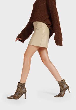 Stivaletti in pelle di serpente con punta affusolata, tacco a stiletto e zip laterale. Il motivo presenta tonalità di marrone e beige con una superficie testurizzata.