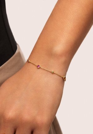 Pulsera de cadena de oro con tres piedras preciosas circulares coloridas: rosa, verde y naranja. La cadena es delicada y tiene una textura suave.