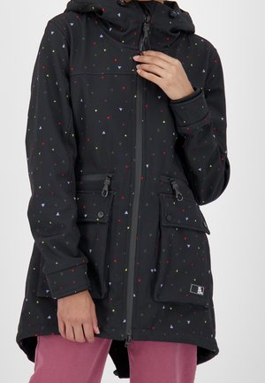 Veste noire à capuche avec de petits motifs triangulaires colorés, fermeture éclair frontale et grandes poches avant, portée sur un pantalon rose.