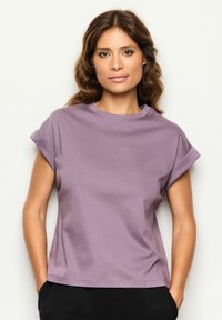 T-shirt viola lavanda a maniche corte con collo rotondo e vestibilità rilassata, realizzata in tessuto liscio e morbido con bordi delle maniche arrotolati.