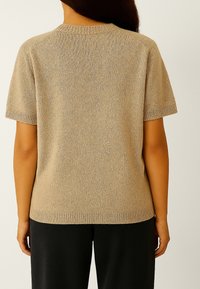 Beige gebreide trui met korte mouwen en een ronde halslijn, met ribgebreide randen en een zachte textuur, gedragen met zwarte broek.