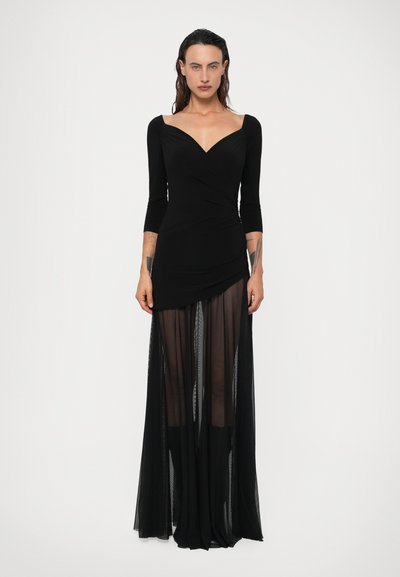Rochie neagră cu un bust ajustat, decolteu adânc în V și mâneci trei sferturi. Fustă transparentă, fluidă, stratificată peste o bază solidă. Textură netedă.