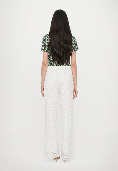Pantaloni larghi bianchi in pizzo abbinati a una maglietta verde a maniche corte con stampa floreale, che mostrano una texture intricata e un design largo.