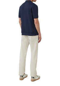 Marineblauwe geribbelde polo met korte mouwen, gecombineerd met off-white broek. De schoenen van het model zijn wit met beige en marineblauwe accenten.