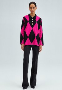 Maglione a motivo argyle in rosa e nero, con colletto e apertura con bottoni dorati; abbinato a pantaloni neri aderenti.