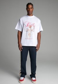 White oversized t-shirt featuring a graphic print, paired with navy sweatpants with side stripes. The outfit includes red sneakers.