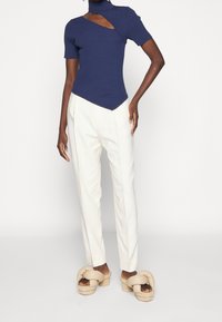 Marineblå åtsittande topp med hög halsringning och asymmetrisk skärning, parat med vita skräddarsydda byxor och beige plattformssandaler.