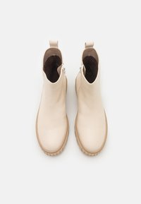 Bottines beiges à la finition en cuir lisse, avec des bouts ronds et des semelles en caoutchouc texturé. Comprend des fermetures éclair latérales doubles et des tirettes.