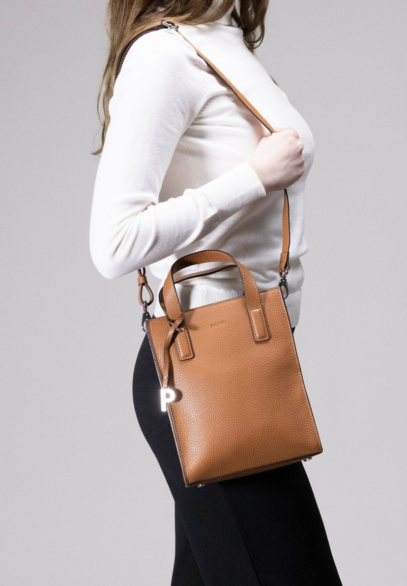 Brown leather handbag with a textured finish, top handles, and a detachable shoulder strap, featuring a minimalistic design and sleek shape.