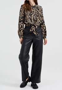 Blus med långa ärmar i svart och beige abstrakt mönster, knuten i midjan. Svarta läderbyxor med vida ben och slät yta. Svarta skor.