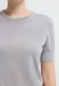 Lys grå striktrøje med korte ærmer og en perlebesat, rund halsudskæring, der har en glat overflade og subtil glans.