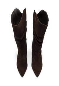 Botas de ante marrón oscuro hasta la rodilla con punta afilada, con el tubo ligeramente caído y cremallera lateral, vistas desde arriba sobre un fondo blanco.