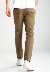 Khaki chinos van katoen met een tapse snit, voorzien van zijzakken en een nette afwerking. Gecombineerd met witte sneakers.