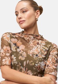 Floral blouse in sheer brown fabric with pastel floral patterns. Features short sleeves and a scalloped neckline detail.