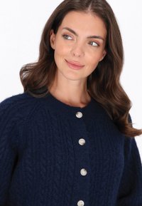 Cardigan lavorato a maglia blu navy realizzato in un materiale morbido e testurizzato, con scollatura rotonda e sei bottoni argentati sul davanti.