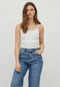 Top de tirantes finos blanco ajustado, combinado con jeans de mezclilla azul de cintura alta. La tela parece suave y los jeans tienen un lavado ligeramente desgastado.