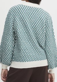 Pull à motifs texturés bleu sarcelle et blanc avec un col et des poignets blancs côtelés, doté d'une coupe ample et de manches bouffantes.