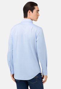 Ljusblå skjorta med lång ärm i bomull, med klassisk krage, rundad nederkant och knäppte ärmslut. Slät textur, minimalistisk design.