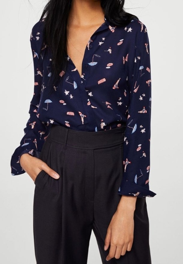 Blusa blu navy con colletto a camicia, caratterizzata da un motivo giocoso di ombrelli e stelle, realizzata in tessuto leggero. Abbinata a pantaloni neri a vita alta.