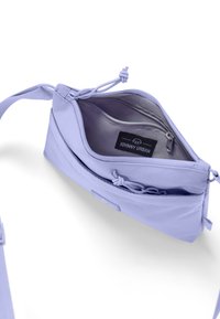 Sac bandoulière lilas avec un tissu texturé, compartiment zippé et bandoulière ajustable. L'intérieur comprend une poche et un label de marque.