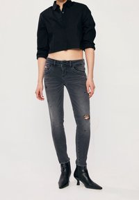 Šedé slim džíny s roztrhanými detaily, spárované s černou zkrácenou košilí na knoflíky a černými špičatými vysokými podpatky.