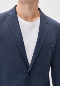Navy blue blazer with a textured fabric, notched lapel, and a single button closure, worn over a plain white t-shirt.