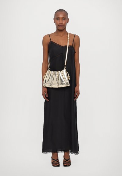 Abito in satin nero con dettagli in pizzo sul corpino e sull'orlo. La modella tiene in mano una borsa plissettata dorata, indossata a tracolla con un sottile strap.