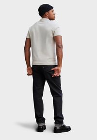 Vaaleanbeige polo-paita, tummat farkut, musta myssy ja mustat kengät. Slim fit -malli, lyhyet hihat ja litteä kaulus. Minimimalistinen muotoilu.