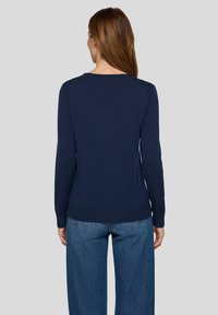 Marineblauer Strickpullover mit langen Ärmeln, geripptem Saum und Rundhalsausschnitt, kombiniert mit weitem Denim-Jeansstoff, Ansicht von hinten.