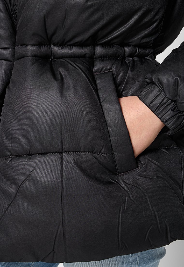 Doudoune noire avec taille cintrée, texture douce, poches latérales et poignets élastiques. Le matériau semble lisse avec une finition brillante.
