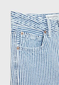 Jean en denim rayé bleu et blanc, avec un bouton en cuivre, une poche avant et une étiquette de marque visible près de la ceinture.
