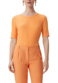 Pomarańczowa bluzka z krótkim rękawem o prążkowanym wzorze i okrągłym dekolcie, zestawiona z dopasowanymi spodniami z wysokim stanem, które mają subtelną teksturę i skrojony krój.