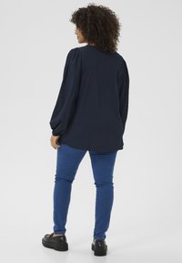 Marineblå langærmet skjorte med quiltede skuldre, parret med tætsiddende blå jeans og sorte platformssko. Letvægts tekstureret stof.