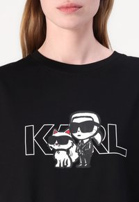 Black cotton t-shirt featuring a graphic of a figure and a cat in sunglasses, with bold white text spelling "KARL" underneath.