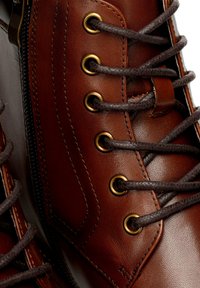 Brązowy skórzany but z złotymi oczkami i ciemnoszarymi sznurowadłami, z precyzyjnym przeszyciem i bocznym zamkiem błyskawicznym ułatwiającym zakładanie.