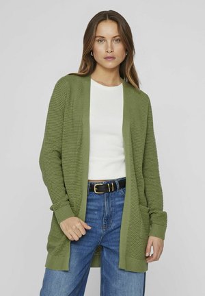 Cardigan verde de punto con mangas largas, frente abierto y patrón texturizado; combinado con una camisa blanca y vaqueros azules.