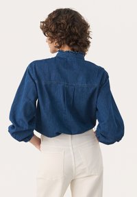 Denim särk volangkraega, sinises värvitoonis ja õhkpuhvikuvarrukatega. Omab taga pleati ja vabalt liibuva lõiget, koos valgete pükstega.