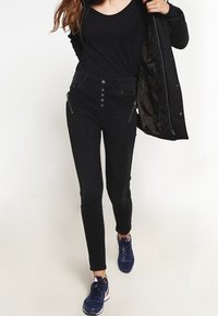 Svarta denim skinny jeans med hög midja, med dragkedjefickor och en rad knappar. Tillsammans med en svart topp och blå sneakers.