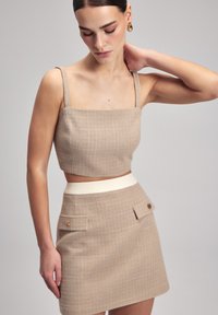 Beige cropped top met vierkante halslijn en dunne bandjes, gecombineerd met een bijpassende beige minirok met zijzakken en een roomkleurige tailleband.