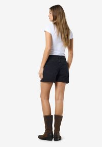 Black denim shorts with rolled cuffs, paired with a fitted white t-shirt and brown knee-high boots. Simple design with back pockets.