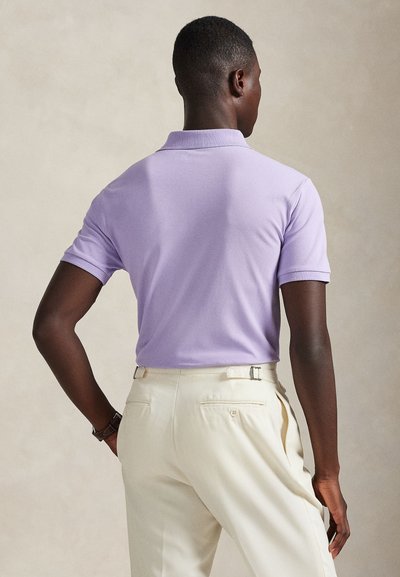 Ανοιχτό μωβ πόλο πουκάμισο με κλασικό γιακά και κοντά μανίκια, σε συνδυασμό με παντελόνια κρεμ χρώματος που διαθέτουν πίσω τσέπες και εφαρμοστή σχεδίαση.